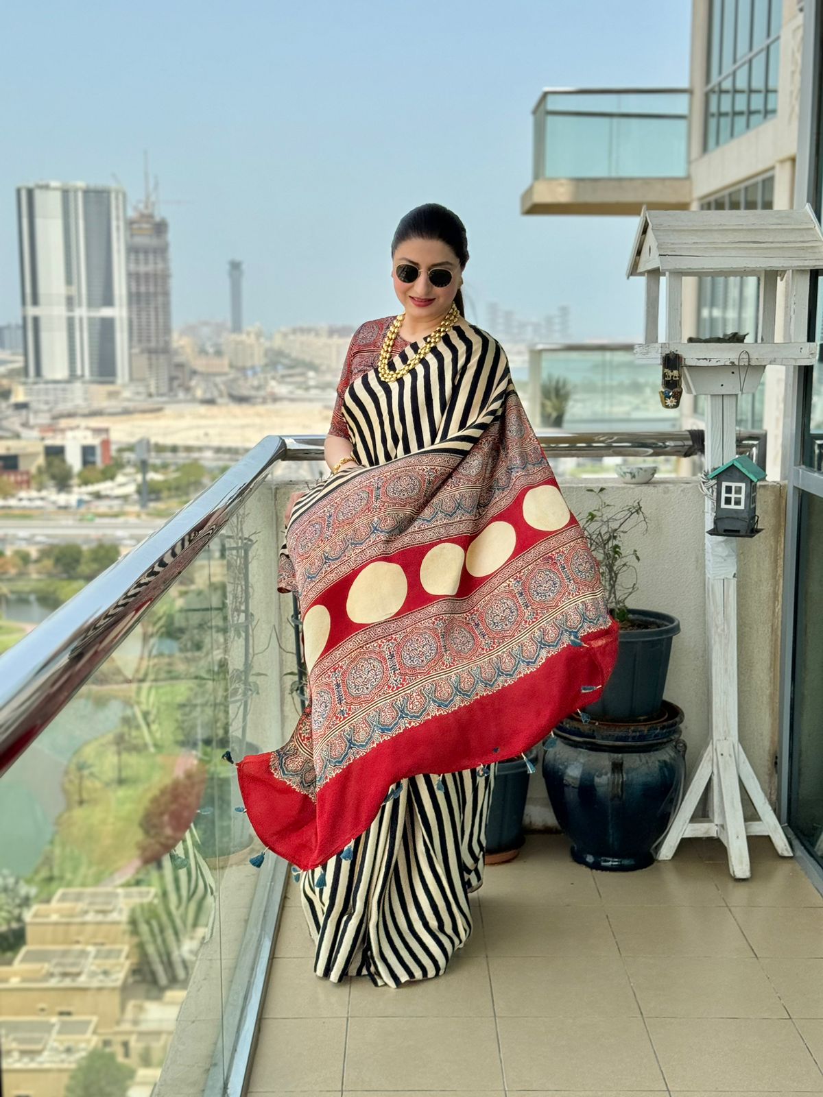 Woman wearing a black and white striped ajrakh saree with red and beige patterned pallu on balcony